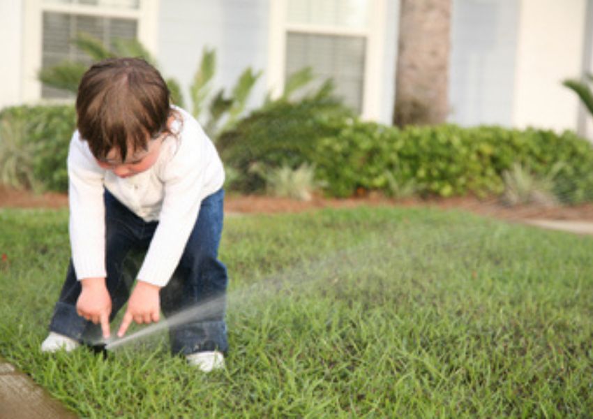 Toddler playing with lawn irrigation sprinkler