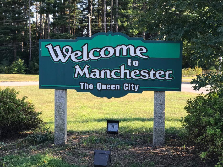 Green wooden sign with Welcome to Manchester - The Queen City
